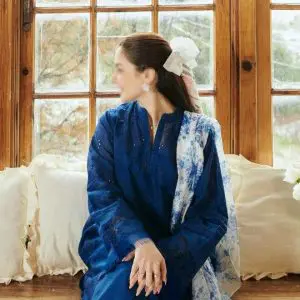 Woman wearing COCO by Zara.J royal blue embroidered lawn suit with printed white-blue dupatta, sitting by a window.