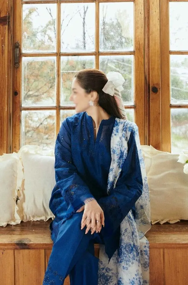 Woman wearing COCO by Zara.J royal blue embroidered lawn suit with printed white-blue dupatta, sitting by a window.